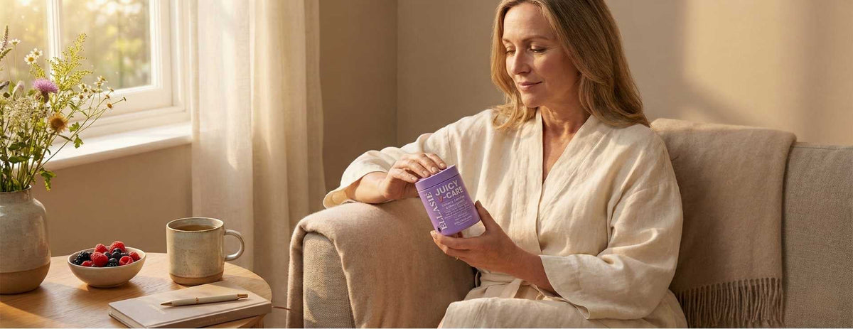 A relaxed mature woman sitting in a sunlit living room, smiling gently while holding and looking at a bottle of Ellasie Juicy V-Care Intimate Comfort supplements.