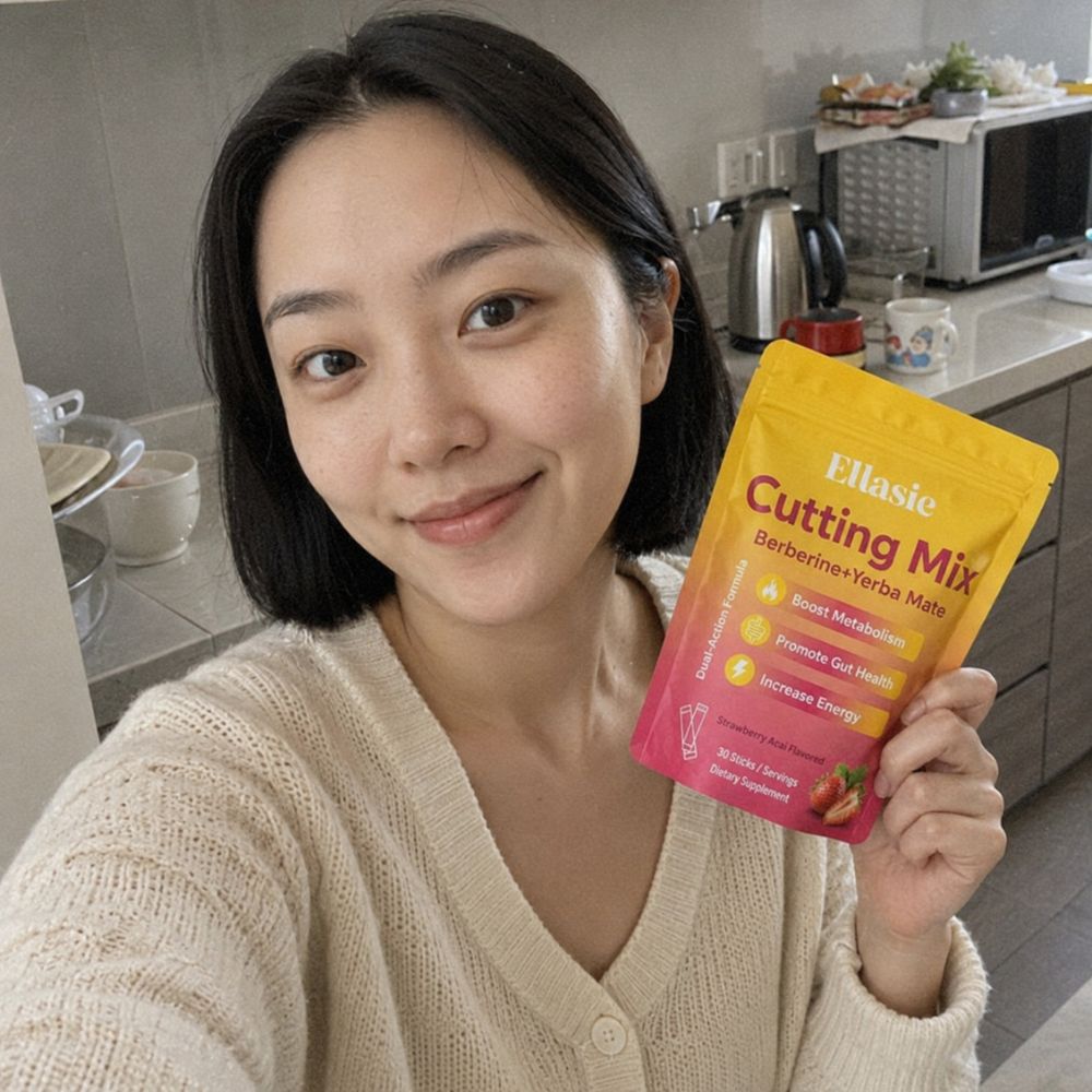 A woman in a beige knit cardigan holds up a yellow and pink pouch of Ellasie Cutting Mix (Barberine + Versa Mate) in a kitchen setting.