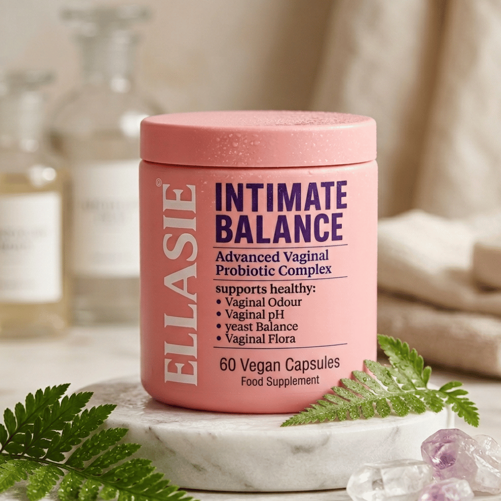 A pink jar of ELLASIE Intimate Balance Advanced Vaginal Probiotic Complex food supplement, styled on a white marble tray with green fern leaves and crystals.