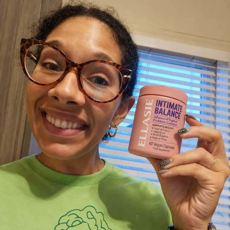 Person holding a pink supplement container labeled 'ELLASIE Intimate Balance' in front of a window.