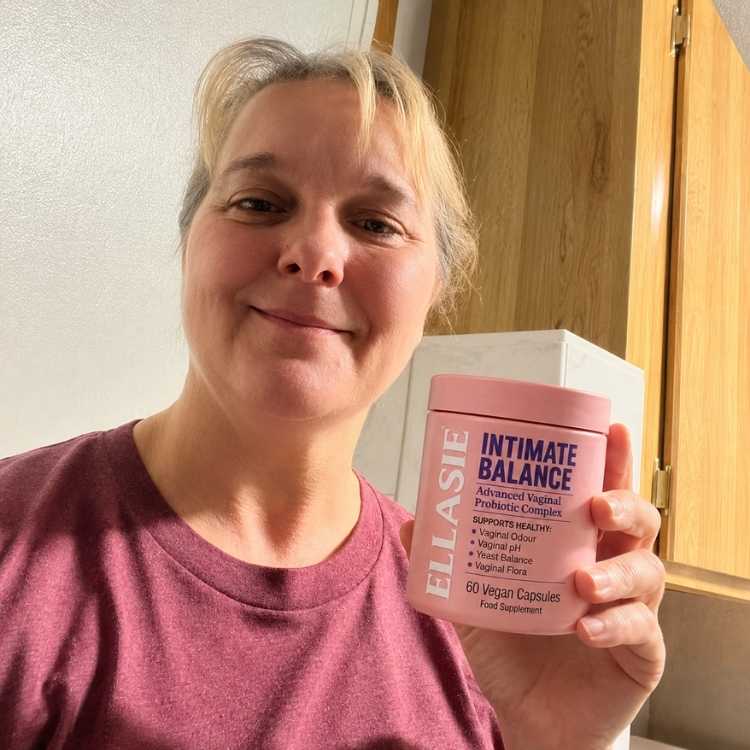 Woman holding a pink container labeled 'Ellasie Intimate Balance' in a kitchen setting.
