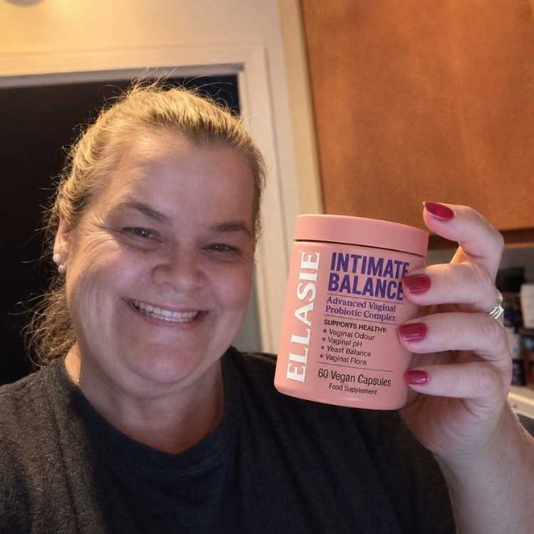 Person holding a pink container labeled 'ELLASIE Intimate Balance' in a kitchen setting.