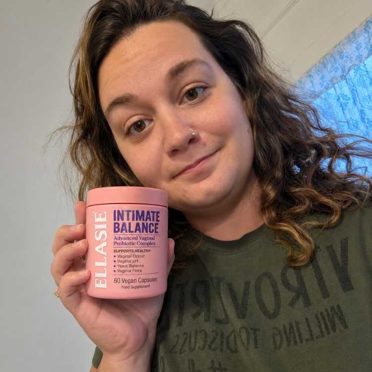 Person holding a pink container labeled 'Ellasie Intimate Balance' against a neutral background