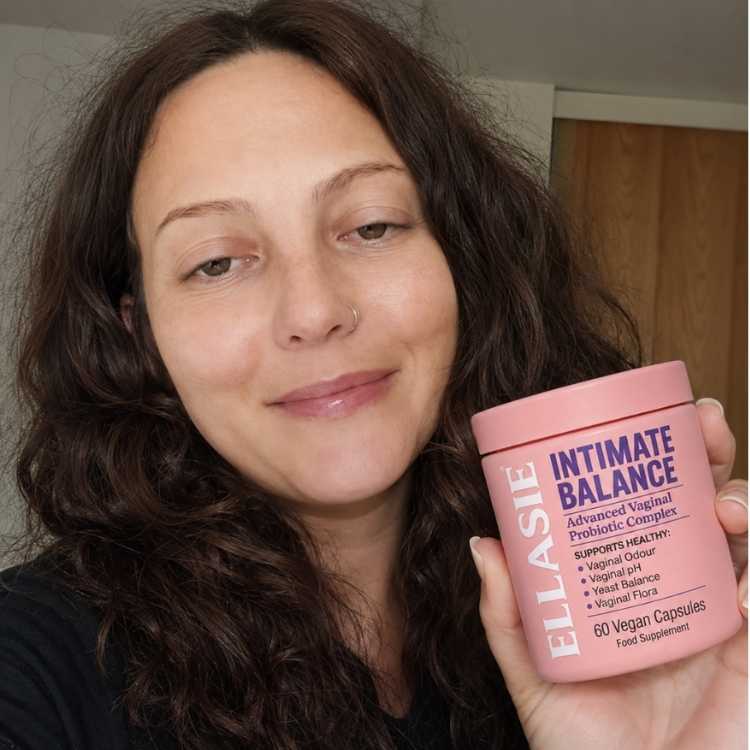 Woman holding a pink supplement container labeled 'Ellasie Intimate Balance' in an indoor setting.