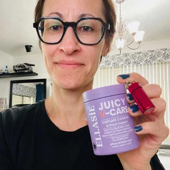 Woman holding a purple container labeled 'Juicy V-Care' and a red object indoors.