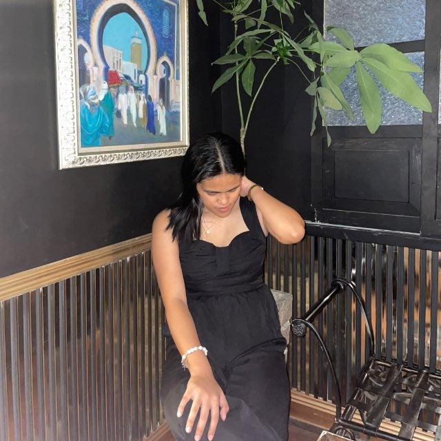 Woman in a black dress sitting in a room with a painting and plant on the wall.