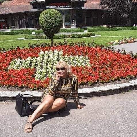 Woman sitting on a path in front of a garden with colorful flowers and a building in the background.