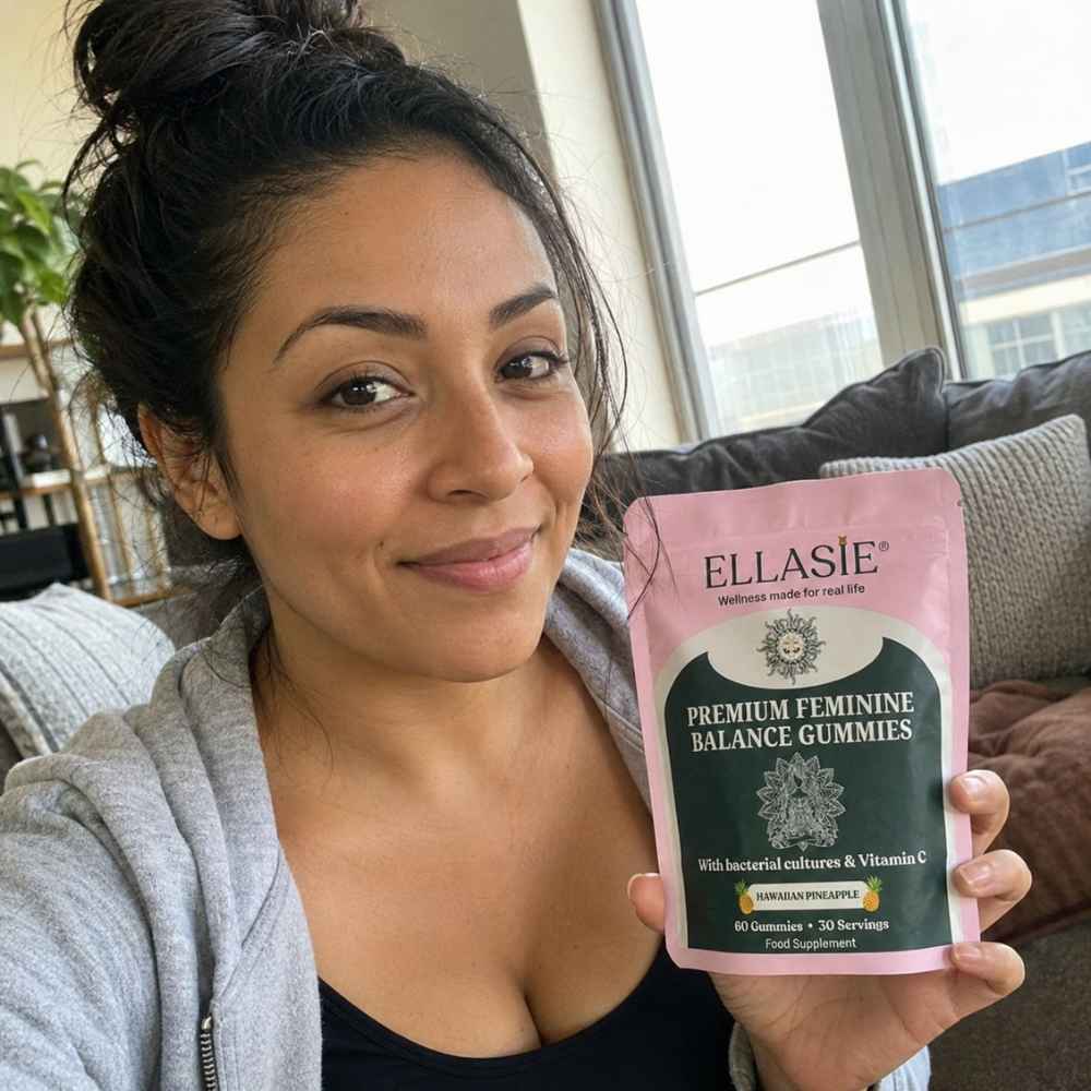 A woman holding a pink and dark green pouch of Ellasie Premium Feminine Balance Gummies in a cozy living room setting.