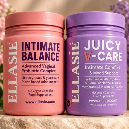 Two supplement jars from ELLASIE on a stone surface, one pink labeled 'INTIMATE BALANCE' and one purple labeled 'JUICY V-CARE', with a softly blurred floral background.